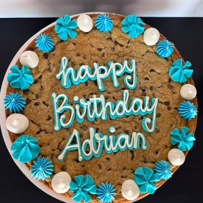 Chocolate chip cookie cake piped with blue buttercream lettering and rosettes